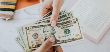 Hands exchanging US dollars on a table with crafting supplies, highlighting financial transactions.