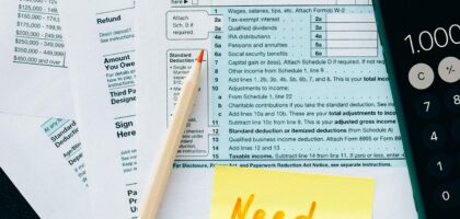 Close-up of tax forms with a calculator and a note asking for assistance.