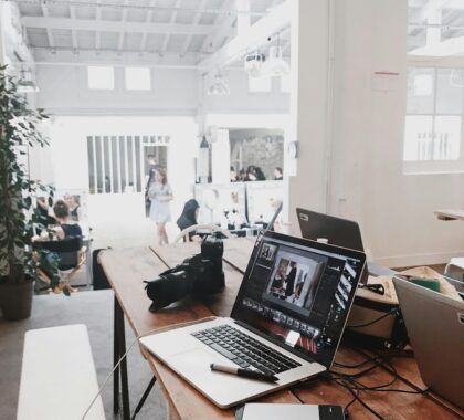 A bright, modern workspace featuring laptops, a camera, and a drawing tablet in an indoor office.